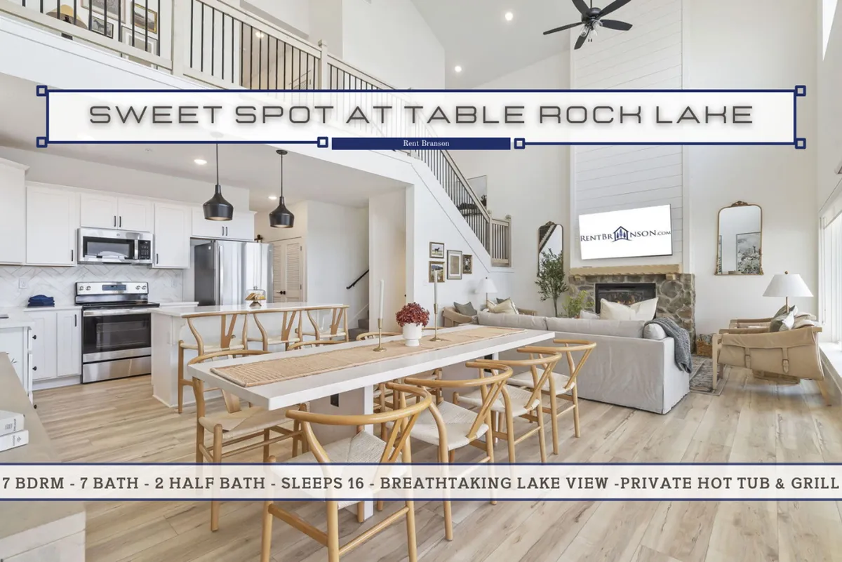 This image captures a spacious, open-concept interior featuring a large dining table, modern kitchen appliances, an open staircase, and a fireplace with a cozy seating area. The space is bathed in natural light, likely streaming in from large windows just out of frame, creating an inviting and communal atmosphere.