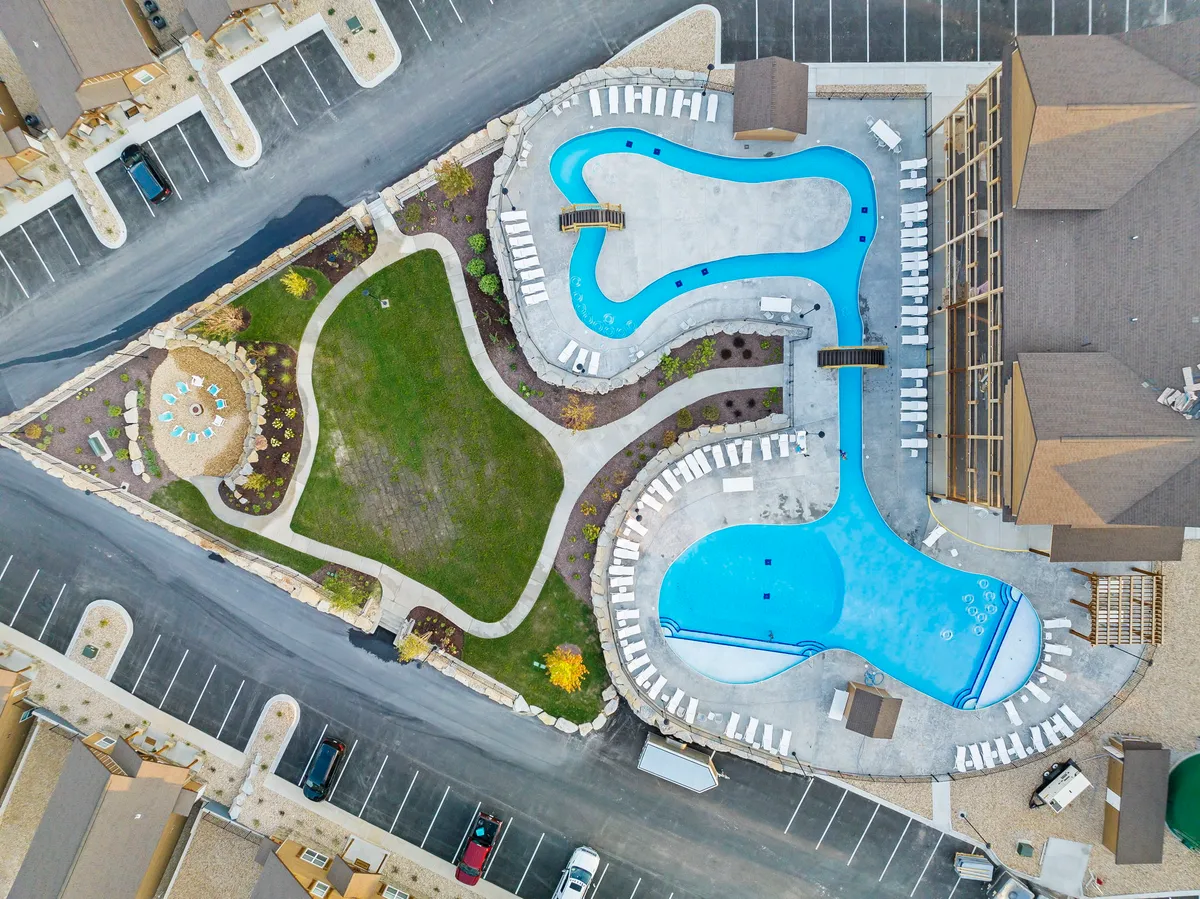 This lively scene displays multiple swimming pools, plenty of lounge chairs, a green lawn, and a beautifully landscaped garden. The area is bustling with activity, illustrating the vibrancy and resort-like feel of the community.