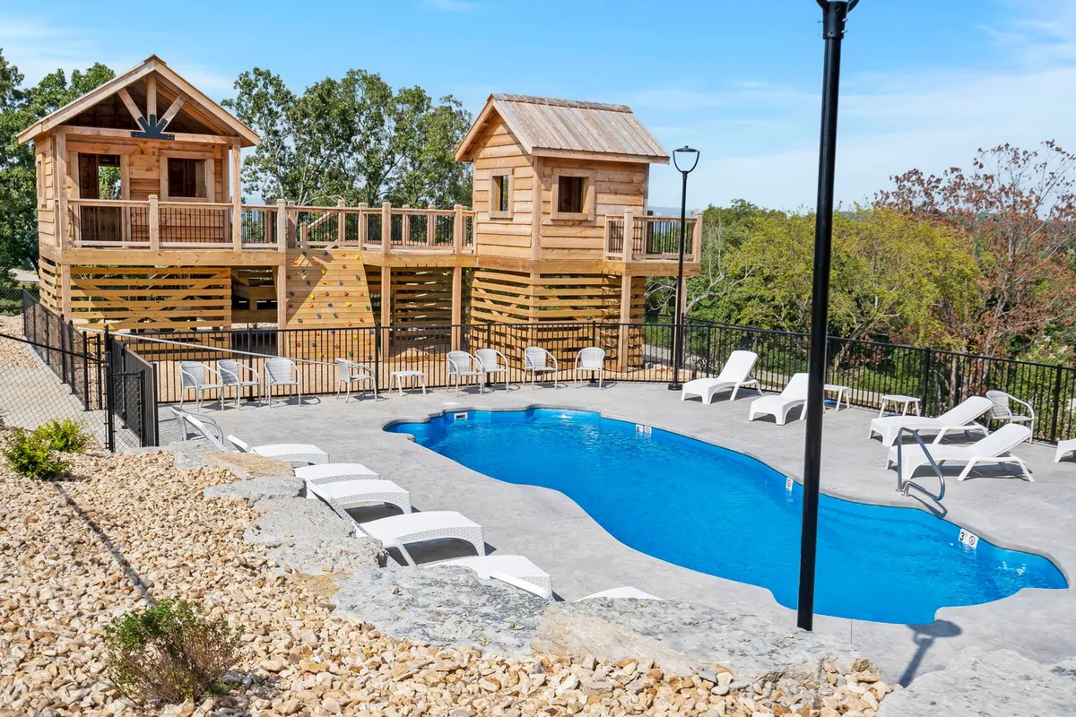 This exterior shot captures a vibrant community pool surrounded by lounge chairs and wooden playhouses, with children playing and families gathered. The lively atmosphere conveys both relaxation and playful energy, with the pool and playground visible in one frame.
