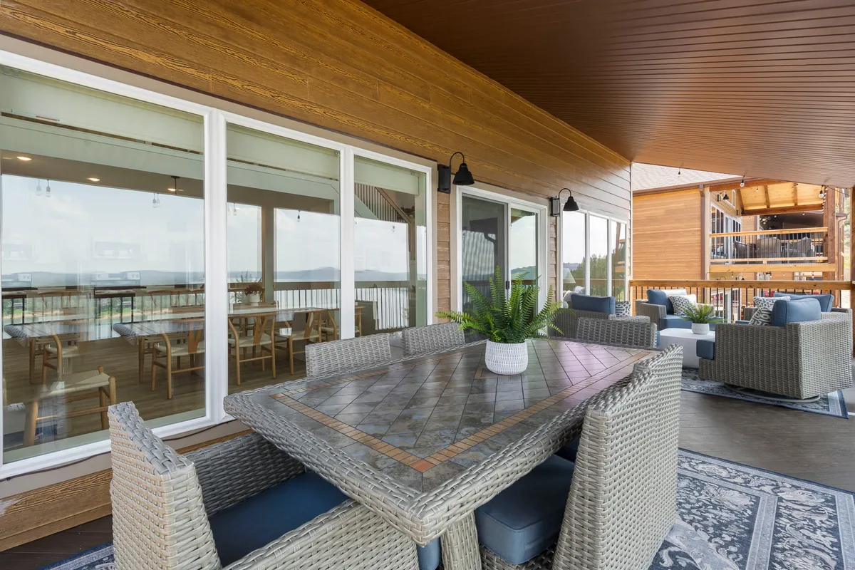 An inviting outdoor dining area set amidst greenery and comfortable seating. The setup overlooks large windows, creating a seamless blend between indoor comfort and outdoor tranquility for guests to dine al fresco or host social gatherings.