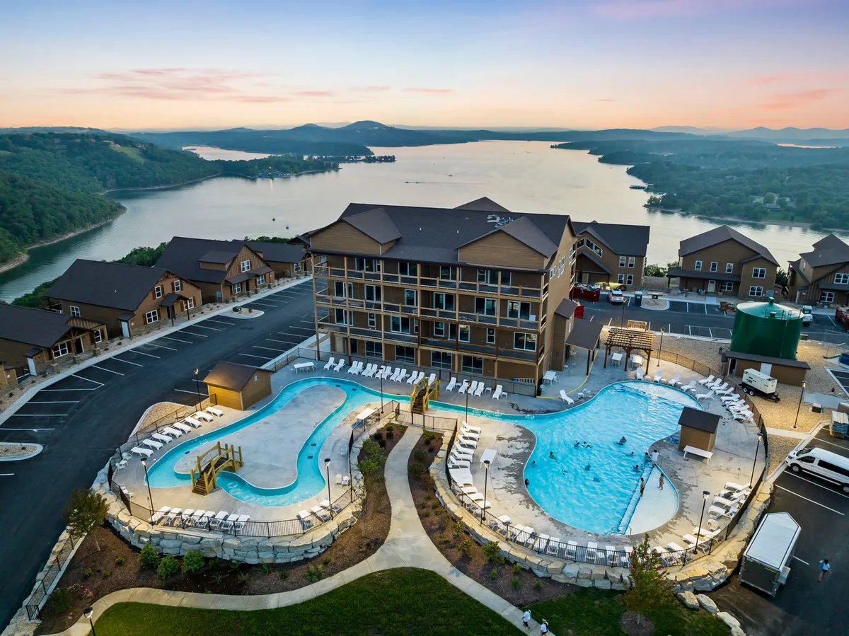 A relaxing pool area that overlooks the lake, with a backdrop of rolling hills and the resort's structure. The scene is set during golden hour, giving it a welcoming, leisurely mood ideal for unwinding after a day of outdoor adventure.