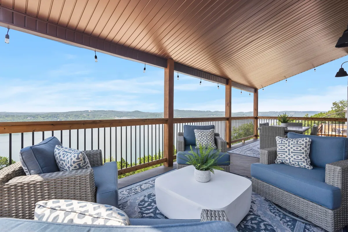 An inviting exterior patio area with comfortable seating, a scenic view of the water, decorative plants, and an area rug. String lights overhead suggest a magical ambiance, perfect for evening relaxation and soaking in a hot tub under the stars.