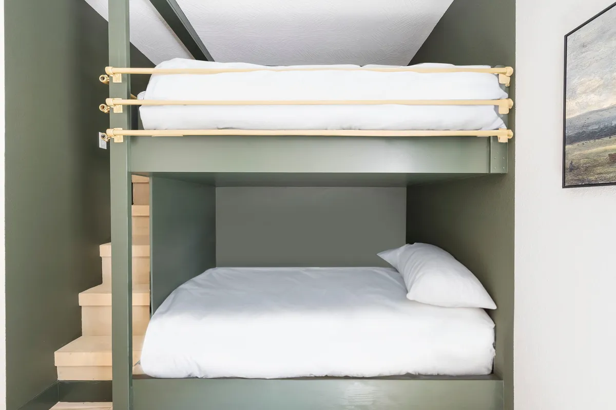 This image shows a custom bunk room featuring built-in bunk beds, a staircase for easy access, and playful wall art. The room is designed to be both inviting and fun for children or groups of kids, with an atmosphere that promotes relaxation and shared experiences.