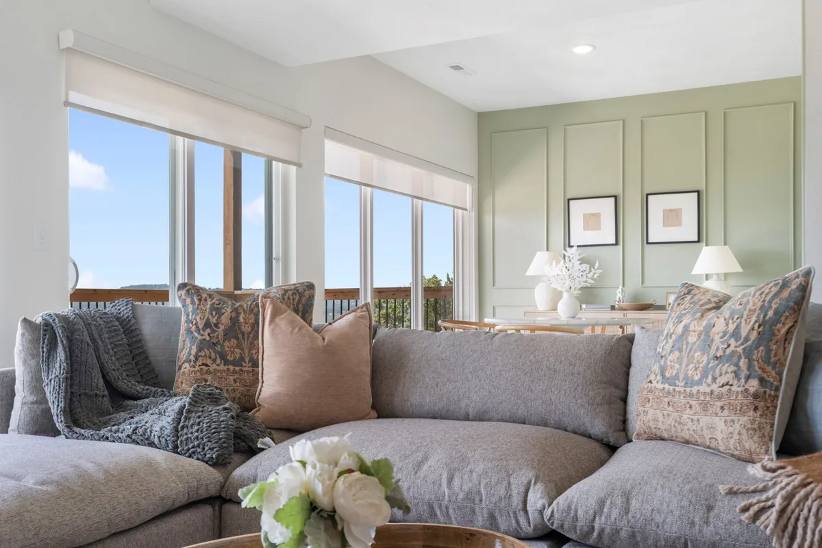 A spacious and inviting lower-level living area with a comfortable sectional sofa, decorative pillows, wall art, and a dining area in the background. The setup is perfect for movie nights, relaxing with family, or gathering for board games and snacks.