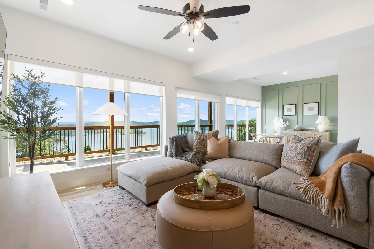 This inviting interior scene features a spacious living area with a large sectional sofa and coffee table, all oriented to maximize the breathtaking, panoramic lake views visible through floor-to-ceiling windows. The cozy setup suggests a perfect spot for gathering, relaxing, and soaking in sunrise vistas over Table Rock Lake.