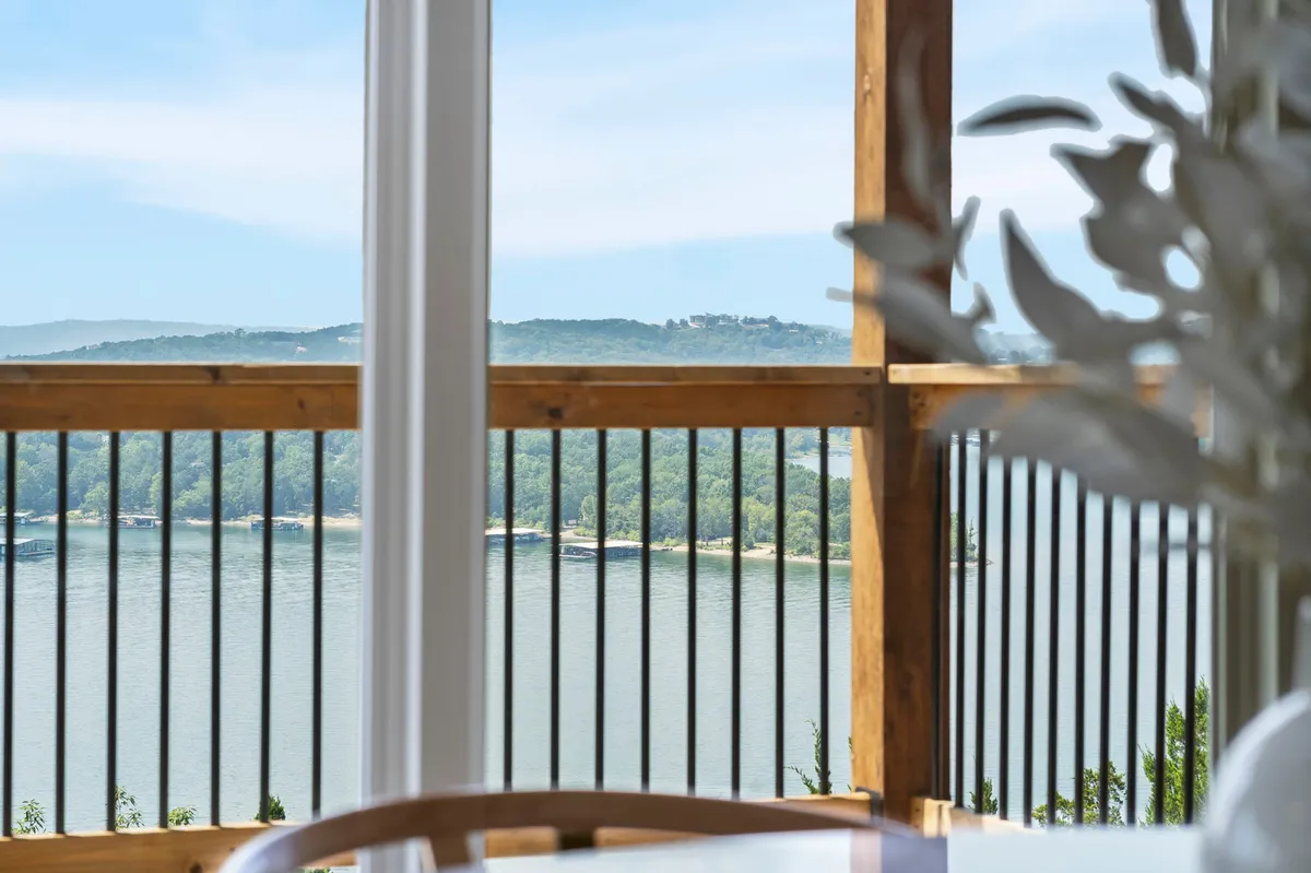 A peaceful lake view framed by a wooden railing with rolling green hills in the background. The balcony space invites guests to relax, entertain, or simply take in the natural beauty of the area, emphasizing serene moments and spectacular scenery.