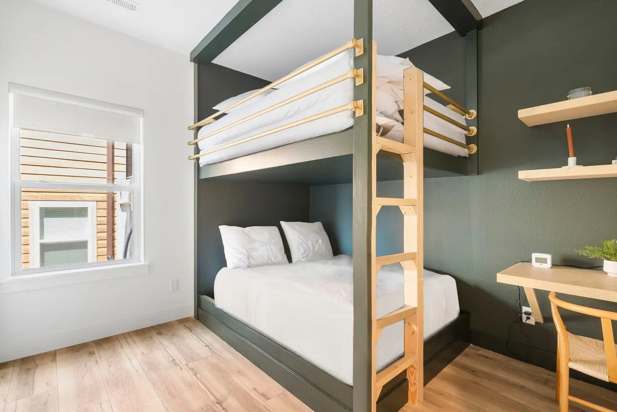 A versatile space with a bunk bed and a built-in desk area beneath a window, letting in natural light. The room is functional and inviting, with both sleeping and work/study options for children or teens.