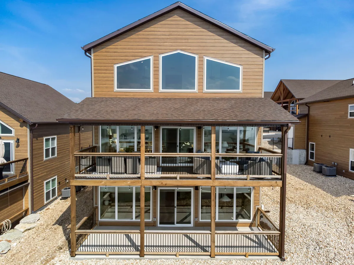 A view of the home's striking modern exterior, featuring large windows that let in natural light and an inviting deck space perfect for outdoor relaxation or gatherings. The wooden structure sets a warm, welcoming tone against the backdrop of nature.