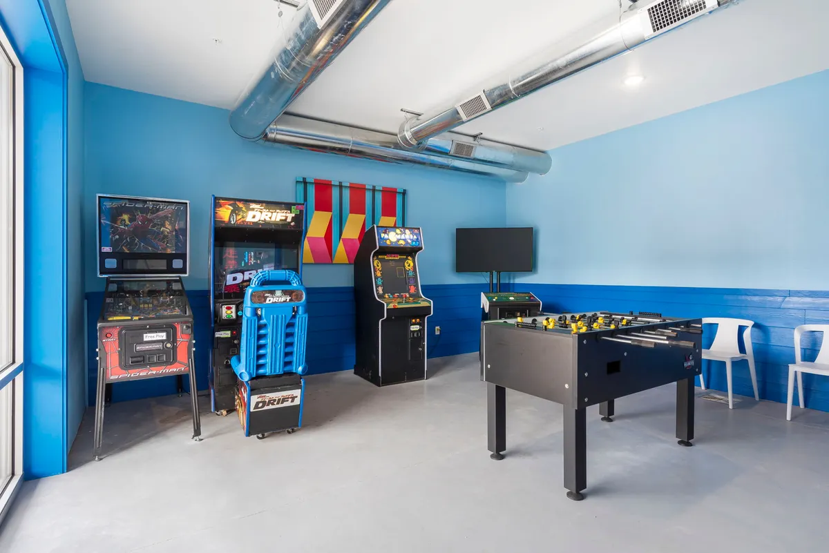 A lively interior entertainment room featuring several arcade machines, a foosball table, and colorful wall decor. The setup invites family members to engage in classic arcade games, socializing, and friendly competition, making it a hub of fun for all ages.